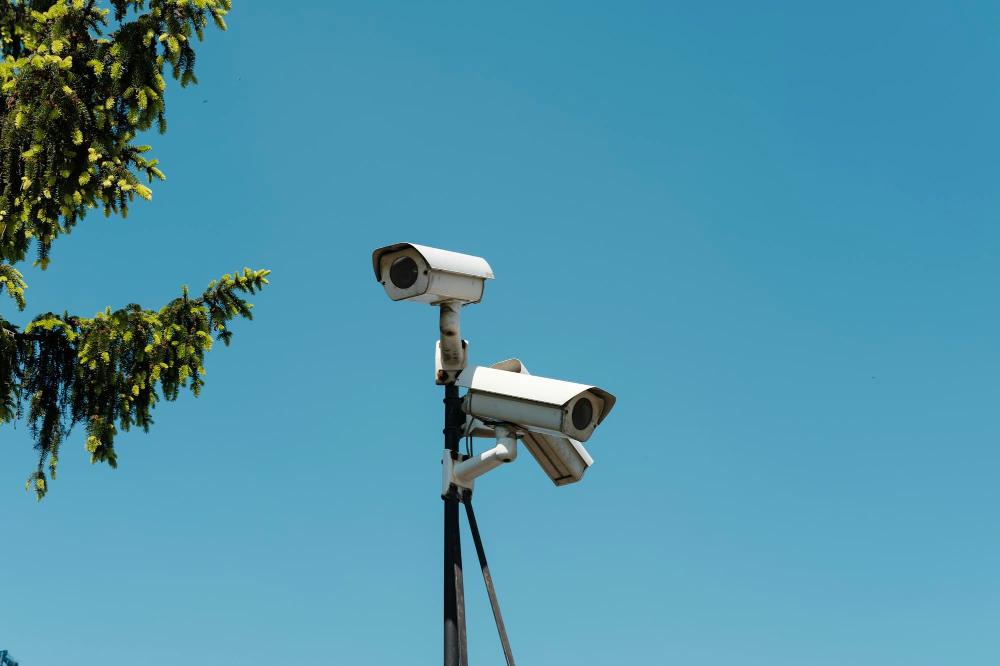Two security cameras on a pole against a blue sky