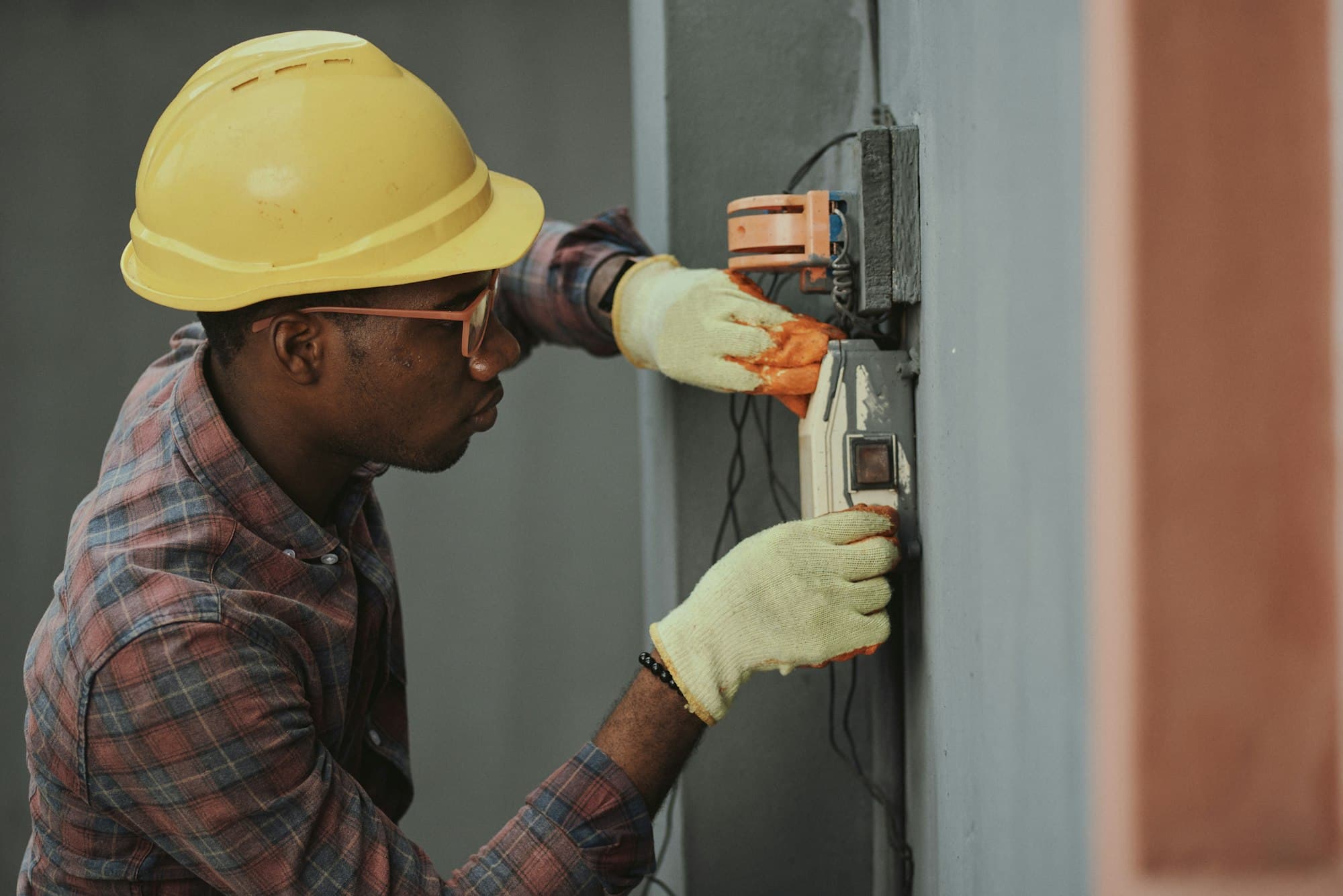 Electrician in a hard hat and gloves working on an electricity meter